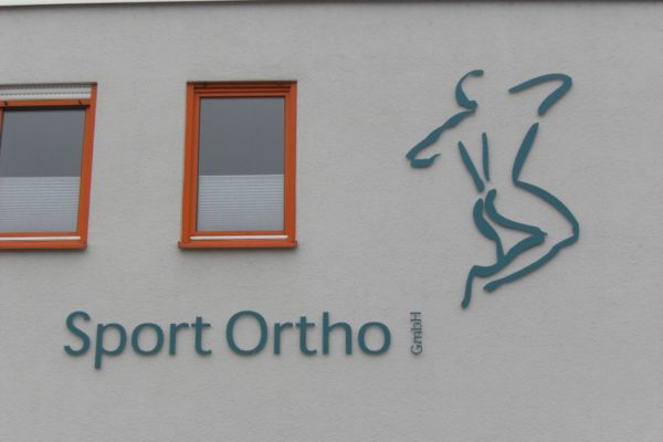 Metallschriftzug + Logo an Betonfassade befestigt